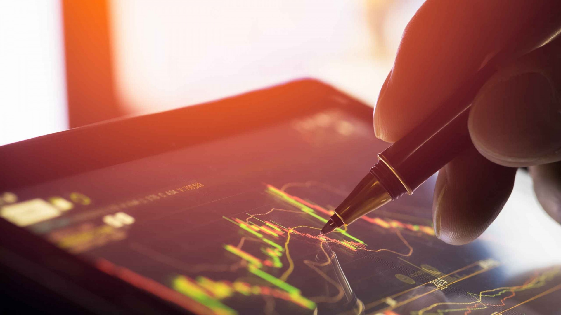 imagem mostra uma caneta apontando um gráfico de bolsa de valores em um tablet