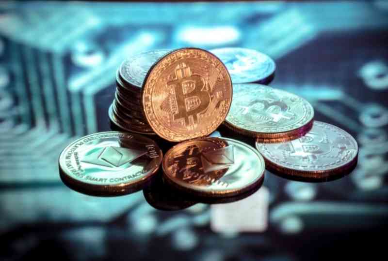 imagem mostra a representação de algumas moedas digitais como o bitcoin e tem o fundo desfocado